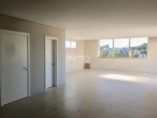Ambiente interno de uma sala ampla com piso claro e grandes janelas.