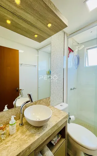 Banheiro com bancada de granito e box de vidro transparente.