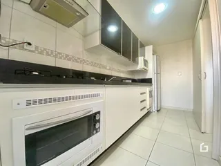Vista da cozinha com armários brancos e revestimento de cerâmica.