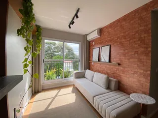 Sala de estar com sofá claro e parede de tijolos aparentes.