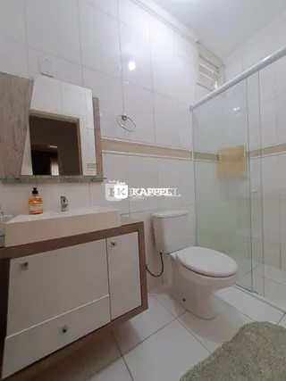 Banheiro com revestimento branco e box de vidro transparente.