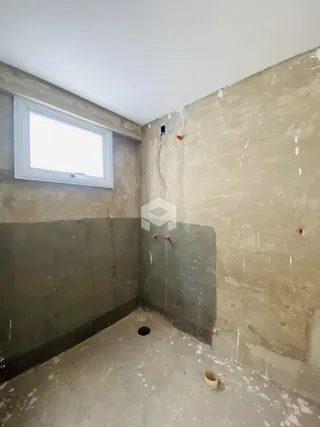 Foto de um cômodo interno com paredes de concreto cru e janela.