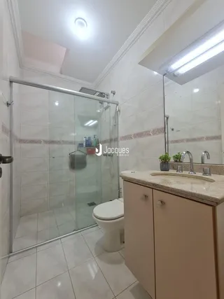 Banheiro com box de vidro e revestimento branco.