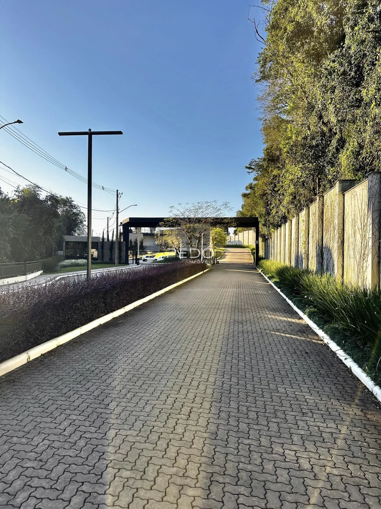Vista da entrada de uma propriedade com um caminho pavimentado e muros laterais.
