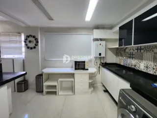 Vista interna de uma cozinha moderna com armários brancos e bancada escura.