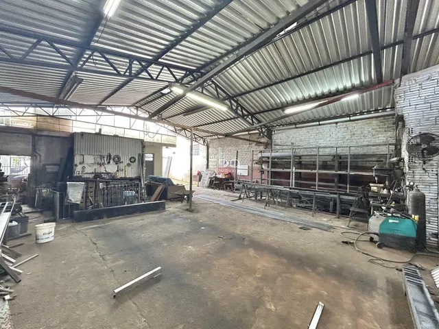 Espaço interno industrial com estrutura de telhado de metal e paredes de tijolo aparente.