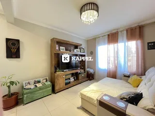 Quarto com cama, televisão e estante de madeira em um ambiente claro.