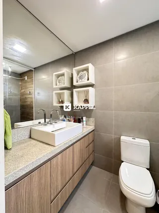 Banheiro com bancada de granito e armários de madeira, apresentando um vaso sanitário branco.
