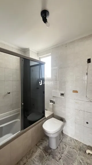 Foto de um banheiro com box de vidro e revestimento de azulejos brancos.