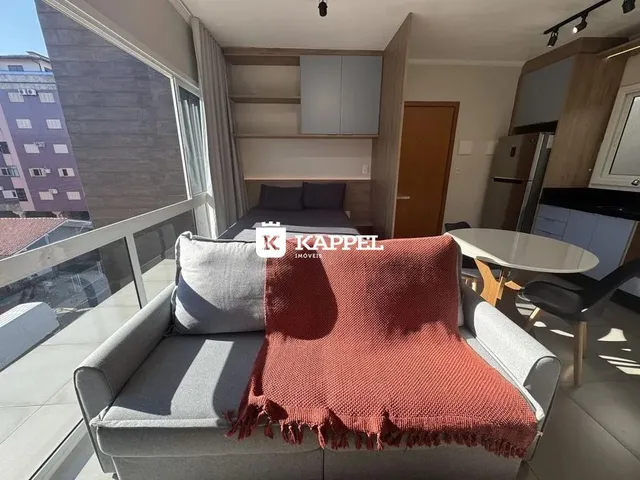 Uma sala de estar com um sofá cinza e manta vermelha é visível na imagem.