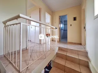 Vista de um corredor com escadaria e piso de cerâmica em uma residência.
