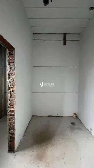 Interior de um cômodo com parede de tijolo aparente e piso cru.