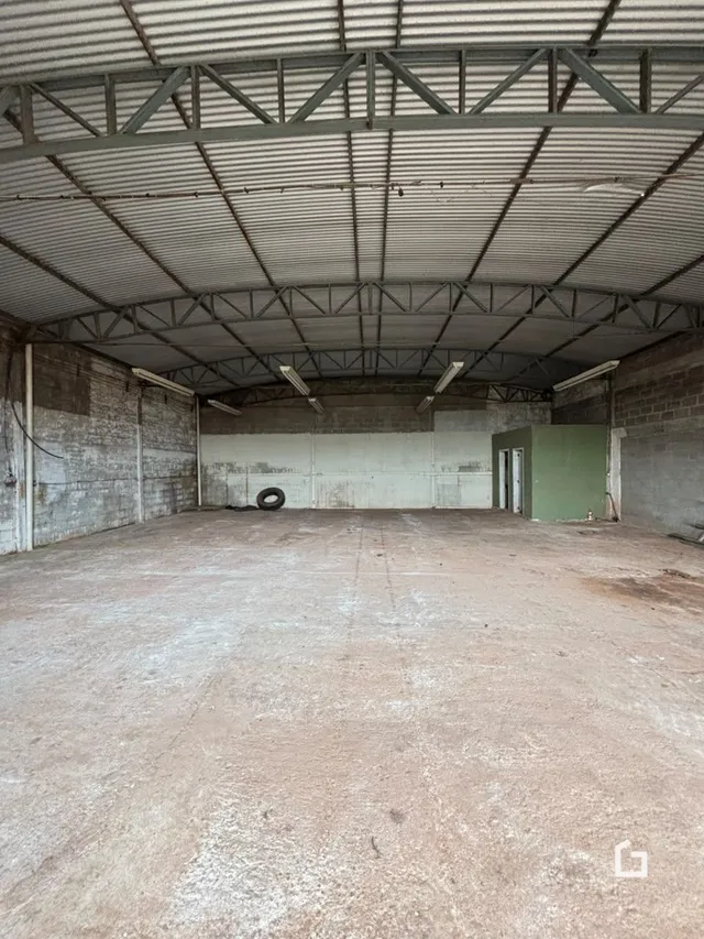 Vista interna de um espaço amplo com estrutura de telhado metálico exposta.