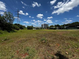 Vista ampla de um campo aberto com vegetação no fundo sob um céu azul com nuvens.