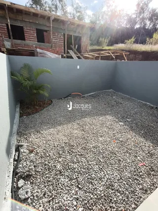 Vista de um terreno com cascalho e uma construção em fase de obra ao fundo.