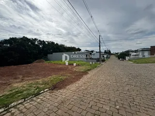 Vista externa de um terreno com uma edificação ao fundo e uma estrada pavimentada.