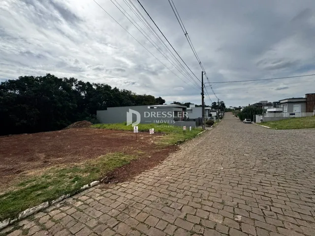 Vista externa de um terreno com uma edificação ao fundo e uma estrada pavimentada.