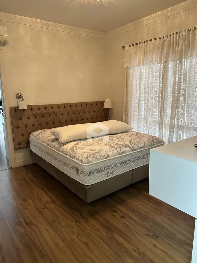 Quarto com cama e janela com cortinas brancas.