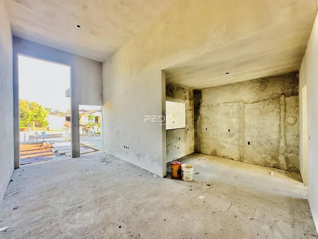 Interior de um espaço com paredes de concreto bruto e abertura para o exterior.