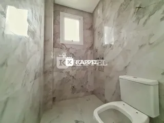 Foto interna de um banheiro com revestimento em mármore claro e vaso sanitário branco.