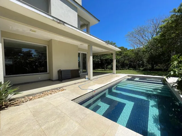 Foto da piscina externa com deck de pedra e área coberta na fachada da residência.