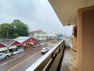 Vista da rua em Lajeado, Brasil, mostrando um prédio e carros estacionados.