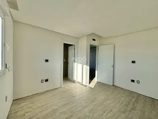 Vista interna de um corredor com piso de madeira clara e paredes brancas.