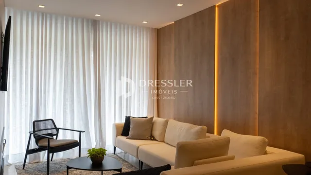 Sala de estar com grandes janelas cobertas por cortinas brancas.