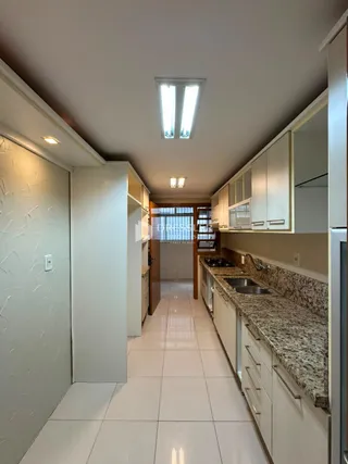 Vista de um corredor interno de uma residência com armários brancos e piso claro.