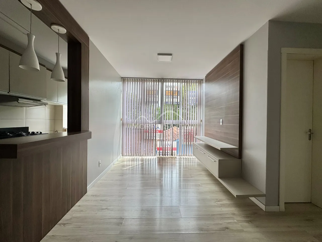 Ambiente interno com piso de madeira clara e área de cozinha moderna.