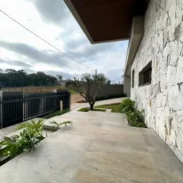 Fachada externa de uma residência com parede de pedra e calçada de concreto.