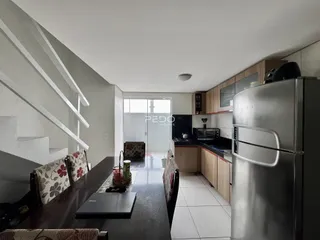 Interior de uma sala de estar com cozinha e escadaria em um imóvel no Brasil.