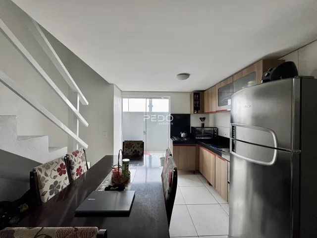 Interior de uma sala de estar com cozinha e escadaria em um imóvel no Brasil.