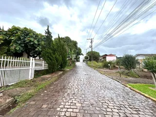Vista da rua pavimentada com cerca branca e vegetação ao longo da propriedade.