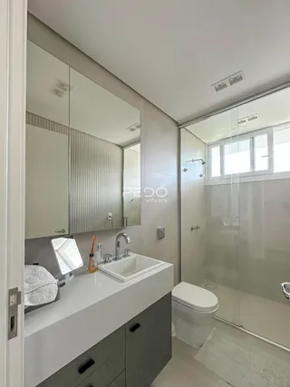 Banheiro moderno com box de vidro e bancada branca.