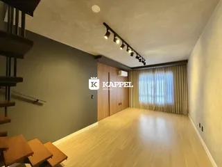 Uma sala de estar com piso de madeira clara e cortinas claras.