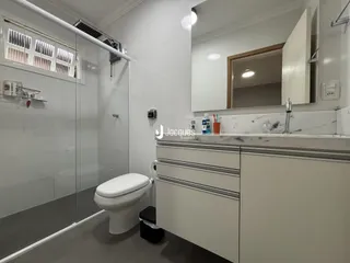 Banheiro moderno com box de vidro e armários brancos.