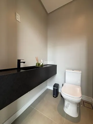 Foto do interior de um banheiro com bancada escura e vaso sanitário branco.