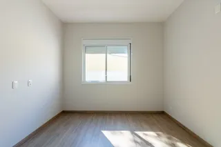 Ambiente interno de uma sala com piso de madeira e janela.