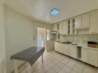 Vista interna de uma cozinha com armários brancos e piso de cerâmica.