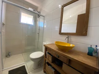 Banheiro com box de vidro, vaso sanitário e bancada de madeira.