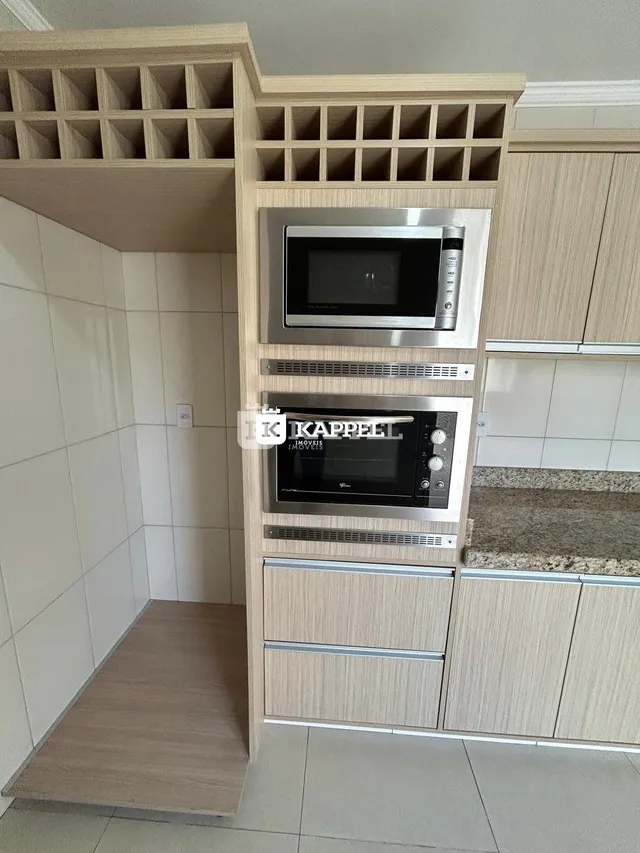 Uma estrutura de armários e prateleiras de madeira está instalada na parede da cozinha.