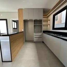 Vista interna de uma cozinha moderna com armários brancos e bancadas escuras.