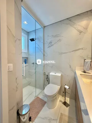 Foto interna de um banheiro com revestimento em mármore e box de vidro.