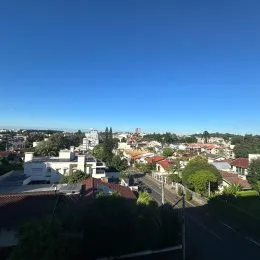 Vista aérea de um bairro residencial em Lajeado, Brasil, mostrando telhados e vegetação sob um céu azul.