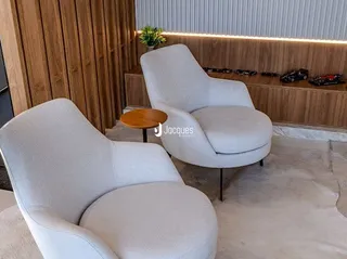 A sala apresenta duas poltronas brancas em um ambiente com painéis de madeira.