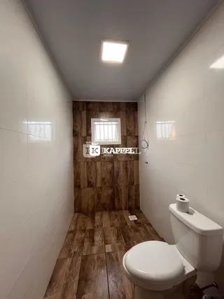 Um corredor com piso de madeira e um vaso sanitário branco são visíveis na imagem.