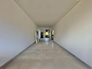 Corredor longo de uma propriedade com paredes brancas e piso de concreto.