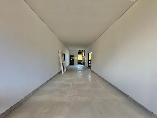 Corredor longo de uma propriedade com paredes brancas e piso de concreto.