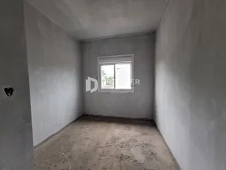 Ambiente interno de uma sala vazia com piso de terra e paredes sem acabamento.